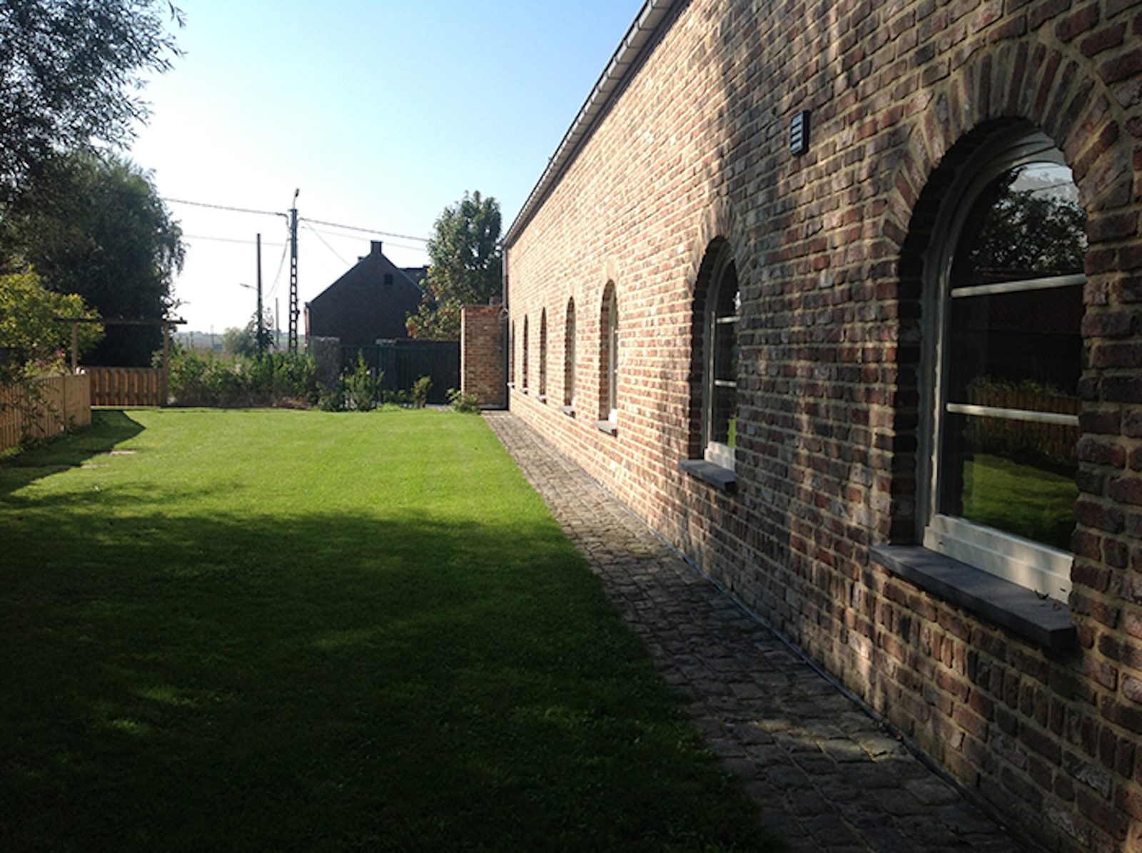 Lange bakstenen hoeve met boogramen, grasperk en bomen